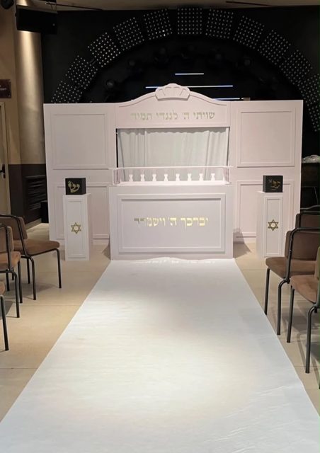 היכל תורה לבן עם פסוקים בזהב, עמודים עם מגן דוד ושטיח לבן לעלייה לתורה
